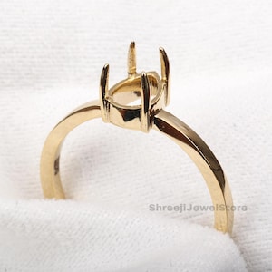 May include: A gold ring setting with prongs designed to hold a gemstone. The ring features a plain band and a detailed setting. The ring is displayed against a white backdrop.