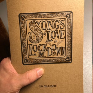 May include: A brown paper book cover with a black and white illustration of a title that reads "Songs of Love in Lockdown" with a decorative border. The author's name, "Ed Gillespie", is printed in black at the bottom of the cover.