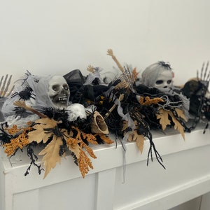 May include: A Halloween mantel decoration with a black, white, and gray color scheme. The decoration features a skull, spider webs, and black branches. The decoration is on a white mantel.