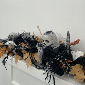 May include: Halloween decoration with a black chain, a white skull, a skeleton, black spiders, and brown leaves.