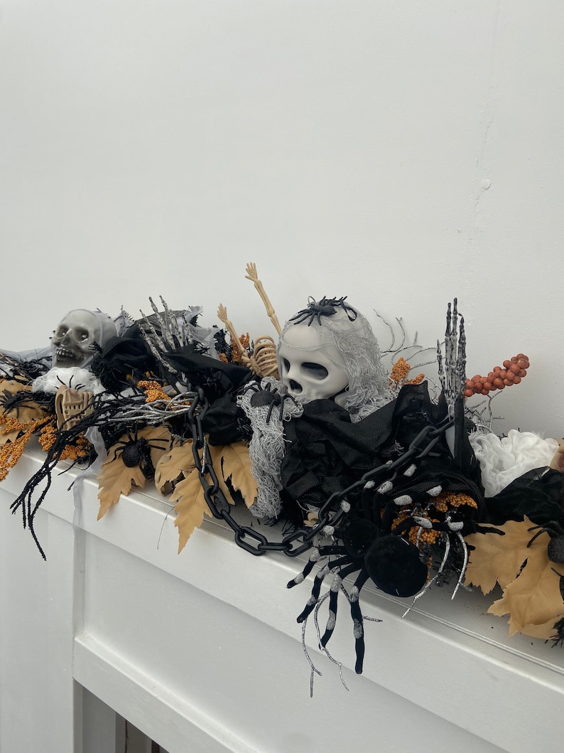 May include: Halloween decoration with a black chain, a white skull, a skeleton, black spiders, and brown leaves.
