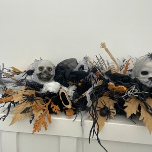 May include: A Halloween centerpiece featuring a black, white, and gold color scheme. The centerpiece includes a skull, spider webs, and a skeleton arm.