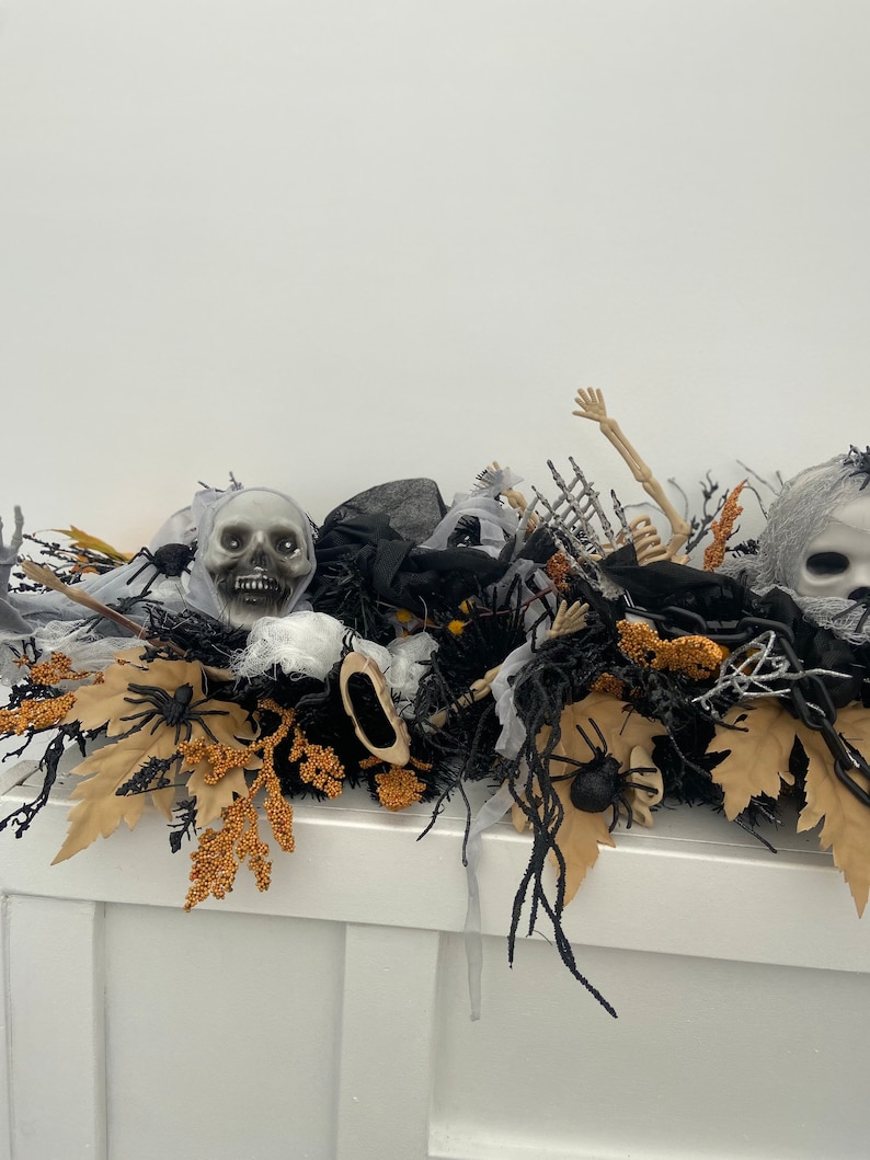 May include: A Halloween centerpiece featuring a black, white, and gold color scheme. The centerpiece includes a skull, spider webs, and a skeleton arm.
