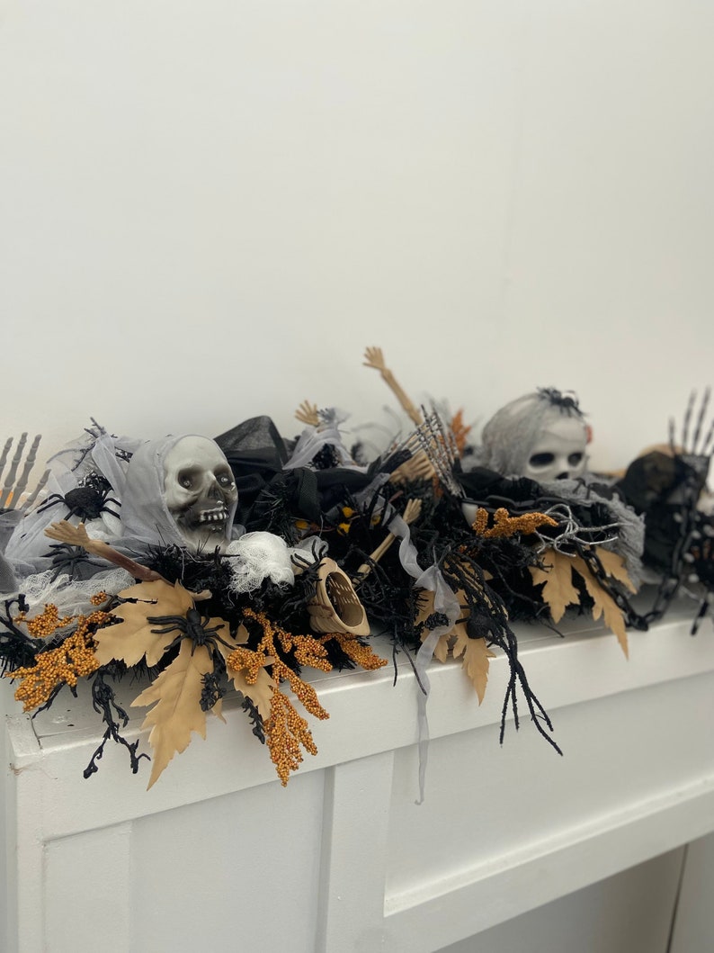 May include: A Halloween mantel decoration with a black, white, and gray color scheme. The decoration features a skull, spider webs, and black branches. The decoration is on a white mantel.