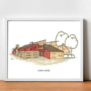 May include: A framed art print of a building with red and tan walls, a red roof, and a sign. Two trees are to the right of the building. The text "DARK HORSE" is at the bottom of the print.