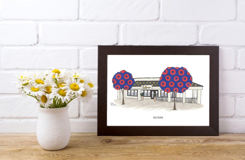 May include: A framed illustration of a restaurant called "Esters" with a blue and red patterned tree on each side of the building. The text "Esters" is written below the building.