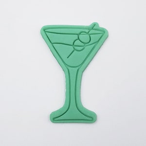 May include: Green plastic cookie cutter shaped like a martini glass with an olive on a stick.