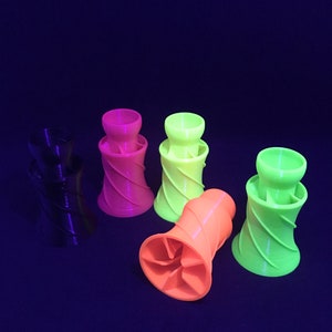 May include: Five 3D printed, spiral-shaped, colorful cups. The cups are black, pink, green, and orange. The cups are arranged in a semi-circle on a dark blue surface.