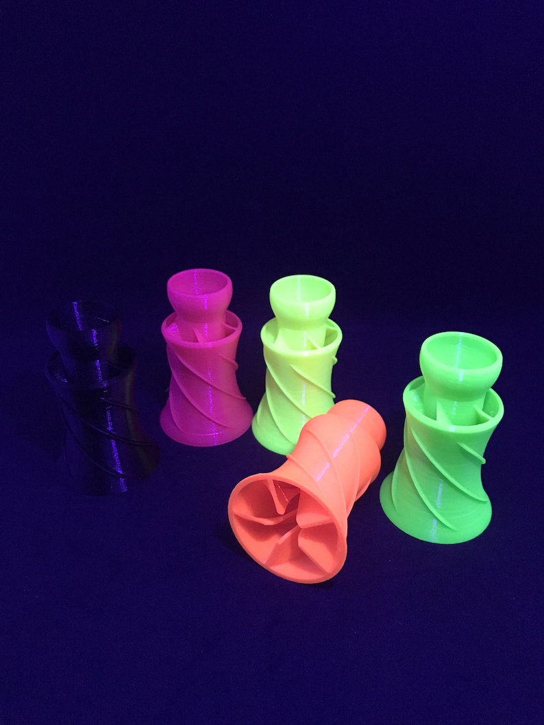 May include: Five 3D printed, spiral-shaped, colorful cups. The cups are black, pink, green, and orange. The cups are arranged in a semi-circle on a dark blue surface.