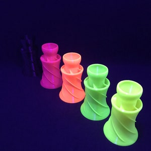 May include: Four 3D printed, spiral-shaped, colorful cups. The cups are in shades of pink, orange, yellow, and green. The cups are arranged in a row from left to right, with the pink cup on the left and the green cup on the right.