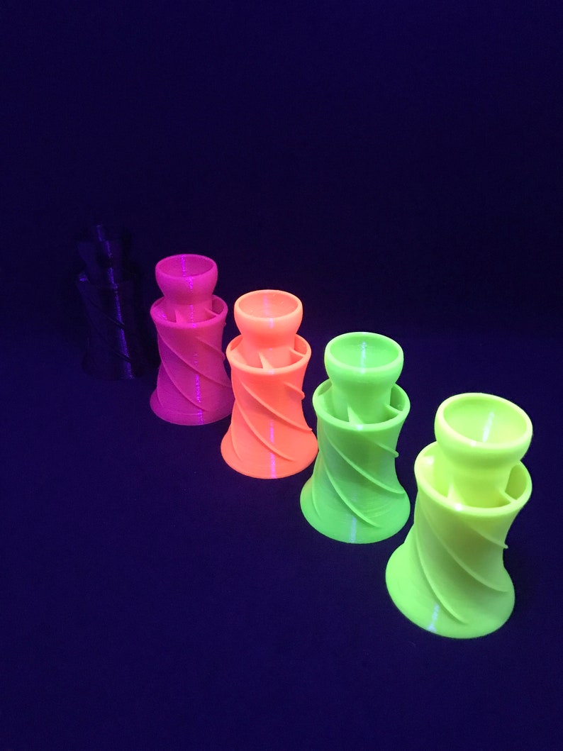 May include: Four 3D printed, spiral-shaped, colorful cups. The cups are in shades of pink, orange, yellow, and green. The cups are arranged in a row from left to right, with the pink cup on the left and the green cup on the right.