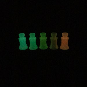 May include: Six small, clear glass bottles with a twisted design. The bottles glow in the dark, with colors ranging from green to orange.