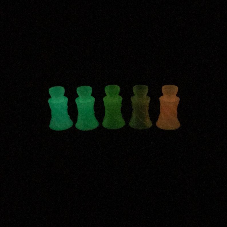 May include: Six small, clear glass bottles with a twisted design. The bottles glow in the dark, with colors ranging from green to orange.