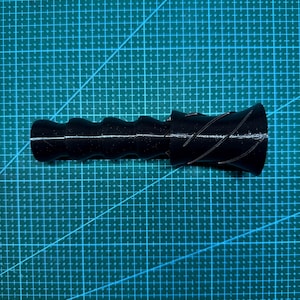 May include: A black, cylindrical object with a textured handle and a flared end. The handle has a series of ridges, and the flared end features diagonal grooves. The object appears to be made of a solid, possibly plastic, material.