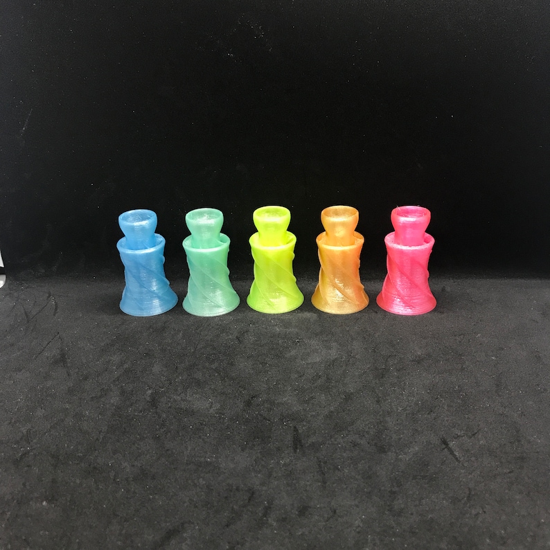 May include: Six small, iridescent glass candle holders in a rainbow gradient. The holders are in a row from left to right: light blue, green, yellow, orange, pink, and red.