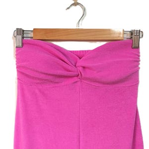 May include: A vibrant pink tube top with a twisted knot detail at the bust, displayed on a wooden hanger. The fabric looks soft and stretchy, with a gathered effect at the top.