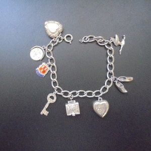 Könnte beinhalten: Silbernes Charm-Armband mit verschiedenen Anhängern, darunter ein Herz, ein Schlüssel, ein Schild und Ballettthemen. Das Armband besteht aus silbernen Kettengliedern und hat einen Verschluss. Die Charms sind detailliert.