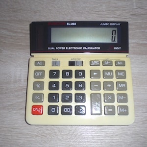 Peut inclure: Calculatrice Busicom EL-203 beige et noire avec un grand écran affichant "0". La calculatrice dispose d'un système électronique à double alimentation et de touches de fonction, dont AC, OFF, %, et des touches numériques.