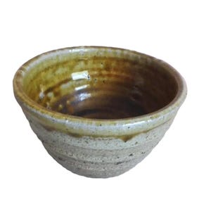 May include: A small, white ceramic bowl with a brown glaze on the inside. The bowl has a slightly rounded shape and a textured exterior.