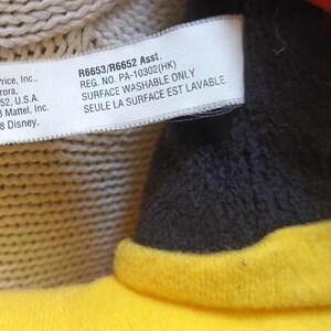 May include: Close-up of a plush toy's tag with text from Fisher-Price, Inc., including the address in East Aurora, NY, and copyright information for Mattel and Disney from 2008. The tag also includes the text "SURFACE WASHABLE ONLY".