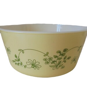 Op de afbeelding: Een gele mengkom met een groen bloemmotief. De kom heeft twee handvatten.