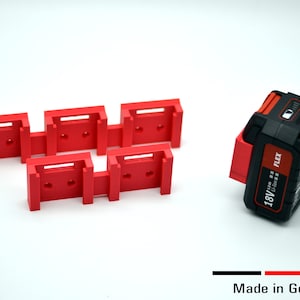Könnte beinhalten: Fünf rote Kunststoff-Batteriehalter für einen schwarzen 18V Li-Ion FLEX Akku. Der Akku ist mit "18V Li-Ion FLEX" beschriftet. Hergestellt in Deutschland.
