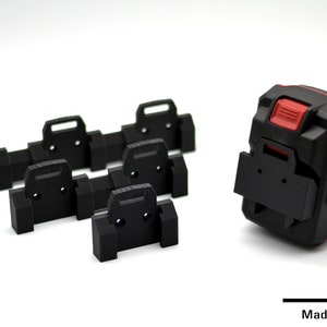 Peut inclure: Cinq supports de batterie en plastique noir avec une batterie rouge et noire sur une surface blanche. La batterie porte l'inscription "POWER X".