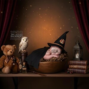 May include: A newborn baby in a wizard costume, lying in a wooden bowl. The scene includes a teddy bear, an owl, books, and a lantern on a shelf, with a burgundy curtain backdrop. The Tiny Atelier Backdrops logo is visible.