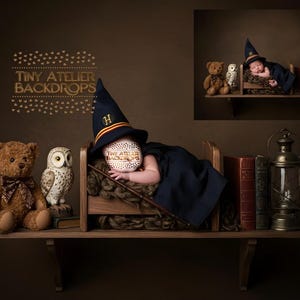 May include: A newborn baby dressed as a wizard, wearing a navy blue hat and cape, lies in a miniature wooden bed on a shelf. A teddy bear, an owl figurine, books, and a lantern complete the scene. The text "TINY ATELIER BACKDROPS" is visible.