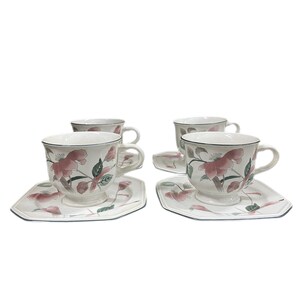 May include: Set of four white teacups and saucers. Each cup and saucer features a floral design with pink flowers and green leaves. The cups have handles and sit on pedestal bases. The saucers are hexagonal with a blue trim.