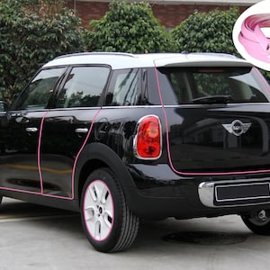 May include: A black Mini Cooper Countryman with pink trim around the edges of the car. The car is parked on a paved surface.