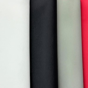 May include: A close-up of four rolls of fabric in white, black, light gray, and red. The fabric has a textured surface and is tightly rolled, showcasing the different colors and textures.