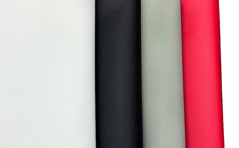 May include: A close-up of four rolls of fabric in white, black, light gray, and red. The fabric has a textured surface and is tightly rolled, showcasing the different colors and textures.