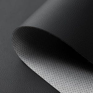 May include: Close-up of a black leather material, partially rolled to reveal a gray, textured underside. The leather has a subtle grain, and the overall effect is one of depth and texture. The image highlights the contrast between the smooth exterior and the patterned interior.