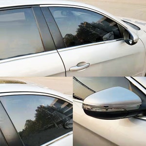 May include: A white car with tinted windows and chrome accents. The car has a side view mirror with a chrome trim. The car is parked on a paved surface.