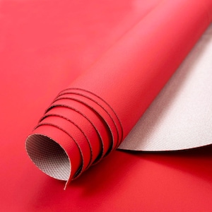 May include: Rolled red leather material with a smooth, glossy finish. The underside of the material is a light gray with a textured pattern. The material is partially unrolled, revealing the interior.