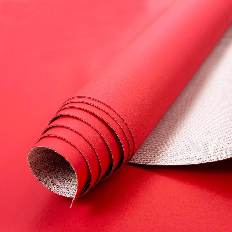 May include: Rolled red leather material with a smooth, glossy finish. The underside of the material is a light gray with a textured pattern. The material is partially unrolled, revealing the interior.