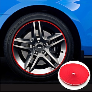 May include: A close-up of a car wheel with a red rim protector installed. The wheel has a silver finish with a five-spoke design. A roll of red rim protector is in the lower right corner. The car is blue.
