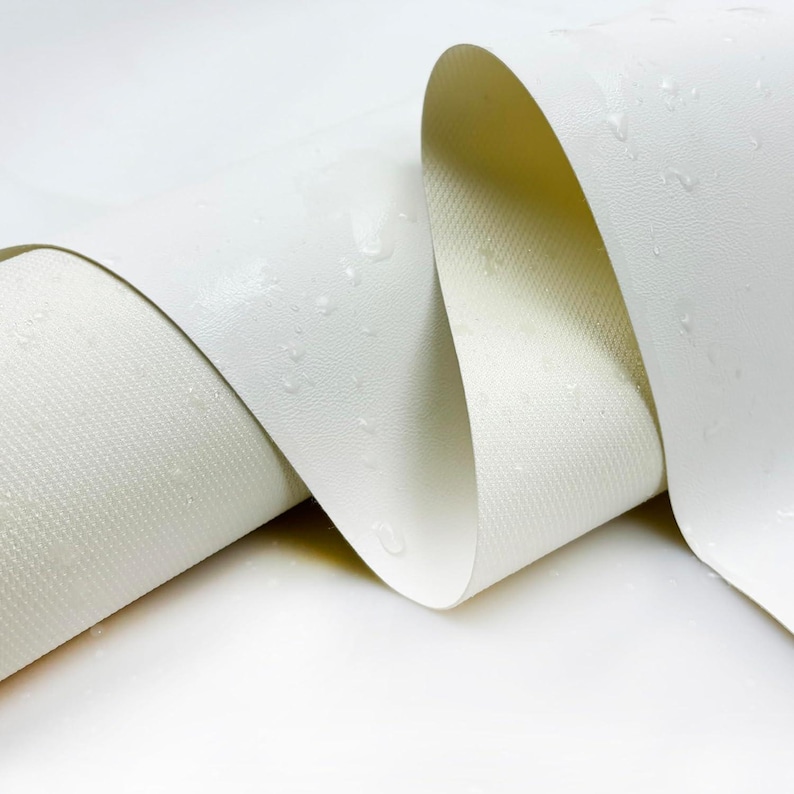 May include: Close-up of a white, rolled fabric with a textured surface. The fabric is slightly curved, revealing both the smooth outer layer and the textured underside. Water droplets are visible on the surface, suggesting a waterproof or water-resistant material.