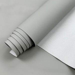 May include: A roll of light gray faux leather material, partially unrolled to reveal the textured surface. The material is smooth and appears to be new, suitable for crafting or upholstery projects.