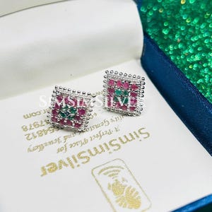 Könnte beinhalten: Quadratische silberne Ohrstecker mit Perlenrand, besetzt mit roten und grünen Edelsteinen. Präsentiert in einer blauen Schmuckschatulle mit dem Text "SimSimSilver".