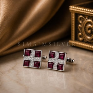 May include: A pair of square silver cufflinks with a cross design. Each cufflink features four square, deep red gemstones and a cross of small, clear gemstones. The text "SIMSILVER" is visible in the background.