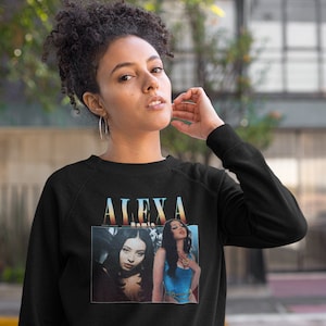 May include: Black crew neck sweatshirt with a vintage-style graphic of a woman and the name "ALEXA" above the image. The graphic has a retro colour scheme. The sweatshirt is made of a soft material.