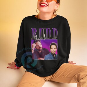 May include: Black sweatshirt with a purple and white graphic of Paul Rudd. The graphic includes the text "Rudd" and a photo of Paul Rudd.