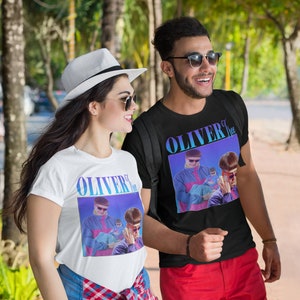 May include: Two people wearing white t-shirts with a graphic print of a person wearing sunglasses and a blue jacket. The text "OLIVER" is printed on the shirts. The person on the left is wearing a white hat and sunglasses. The person on the right is wearing sunglasses and red shorts.