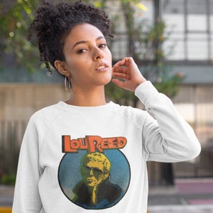 May include: White sweatshirt with a vintage-style graphic of Lou Reed, featuring a blue and yellow background with orange text.