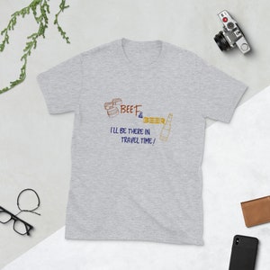 Op de afbeelding: Grijs T-shirt met een afbeelding van een cartoon hamburger en een fles bier. De tekst luidt "BEEF & BEER I'LL BE THERE IN TRAVEL TIME!"