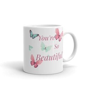 May include: White ceramic mug with a pink and blue butterfly design. The mug has the text "You're So Beautiful!" printed on it.