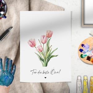 May include: A white card with a bouquet of pink tulips and the text "F&uuml;r die beste Oma!"  A small heart symbol is below the text.