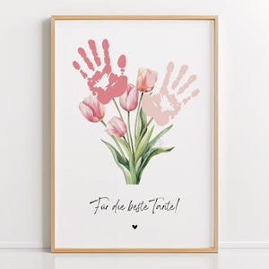 以下が含まれることがあります： ピンクと白の手形のデザインが施された額装されたプリントで、ピンクのチューリップのブーケが描かれています。プリントの下部には「Für die beste Tante!」というテキストがあります。